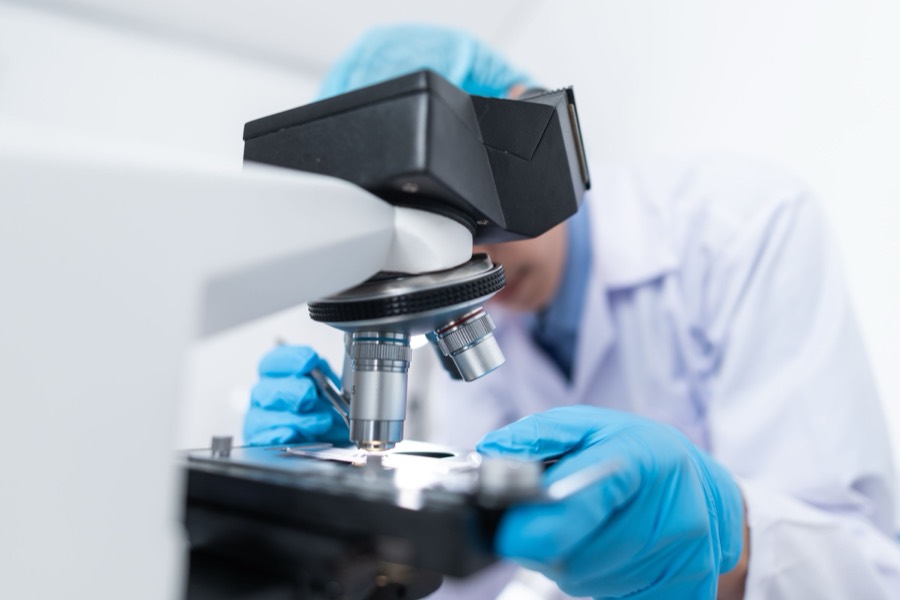 Investigador en bata blanca operando microscopio en laboratorio